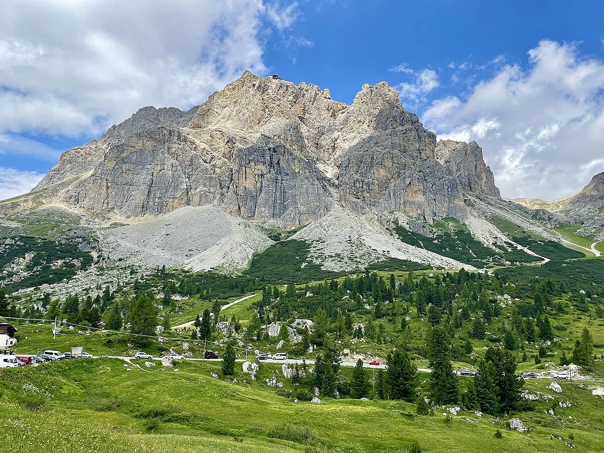 Parete rocciosa delle Dolomiti sopra un prato verde, con le nuvole basse